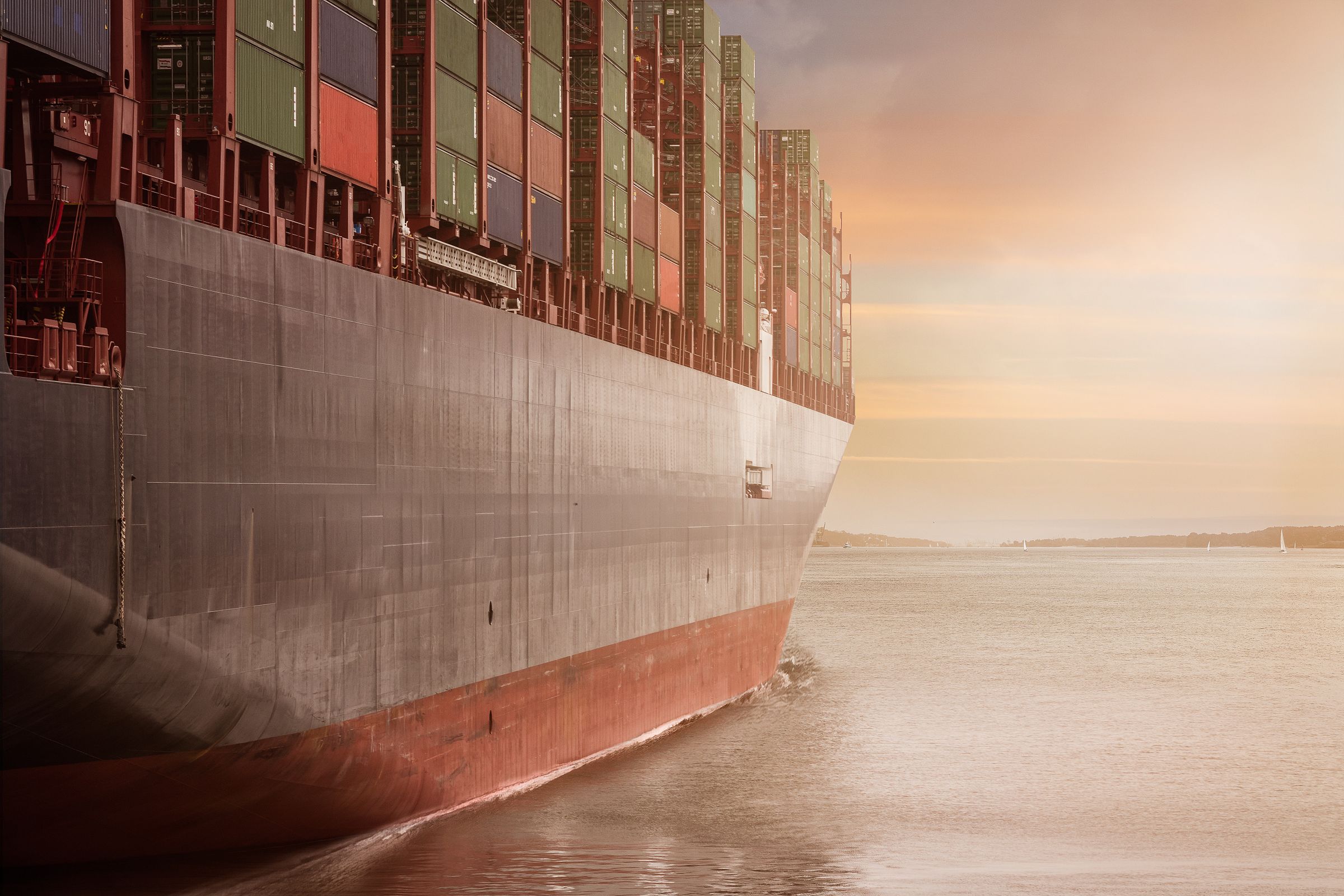 Container ship hull and stacked cargo at dusk